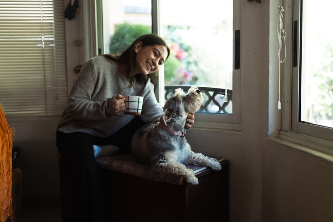 human-animal bond — Woman holding coffee cup petting a dog by window